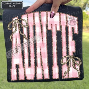May include: Black sweatshirt with the word "AUNTIE" in large pink and white plaid letters outlined with leopard print. Two leopard print bows are on the front. The top left corner has a black box with the words "COMFORT COLORS BLACK".