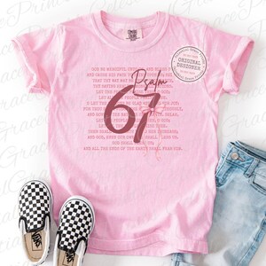 May include: A light pink t-shirt with the text "Psalm 67" and a bow graphic. The shirt also features a list of text. A pair of black and white checkered slip-on shoes are in front of the shirt.