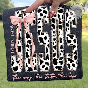 Puede incluir: Camiseta negra con la palabra "JESUS" en un dise&ntilde;o de letras en negrita, con un estampado de vaca y un borde de estampado de leopardo. Un lazo rosa y el texto "Juan 14:6" est&aacute;n en el lado izquierdo. La frase "the way, the truth, the life" est&aacute; en la parte inferior.