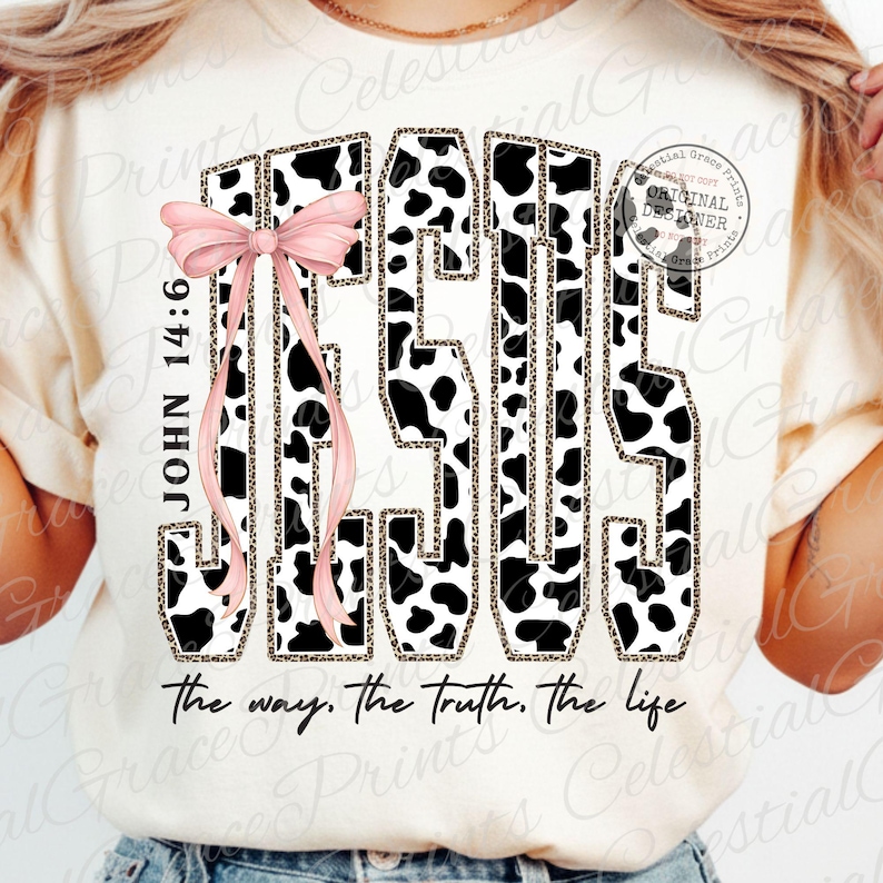 Puede incluir: Camiseta color crema con la palabra "JESUS" en un dise&ntilde;o audaz de estampado de vaca con acentos de estampado de leopardo. Un lazo rosa y el texto "JOHN 14:6" est&aacute;n a la izquierda. La frase "the way. the truth. the life" est&aacute; en la parte inferior.
