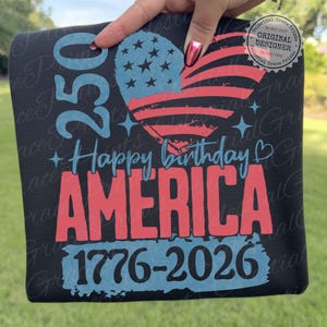Puede incluir: Camiseta negra con un dise&ntilde;o patri&oacute;tico. Presenta una bandera estadounidense en forma de coraz&oacute;n, el texto "Happy Birthday AMERICA", los n&uacute;meros "250" y "1776-2026". El dise&ntilde;o es en rojo, blanco y azul.
