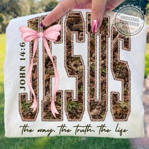 May include: White t-shirt featuring the word "JESUS" in a camouflage and leopard print design, with a pink bow and the text "JOHN 14:6". The phrase "the way, the truth, the life" is printed at the bottom.