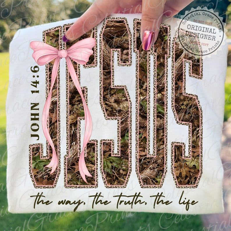 May include: White t-shirt featuring the word "JESUS" in a camouflage and leopard print design, with a pink bow and the text "JOHN 14:6". The phrase "the way, the truth, the life" is printed at the bottom.