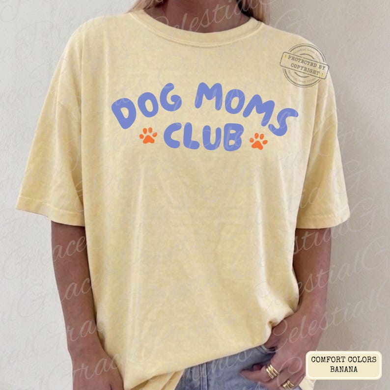May include: A light yellow t-shirt with the text "DOG MOMS CLUB" in blue, with orange paw prints. The shirt is a Comfort Colors brand, banana color.