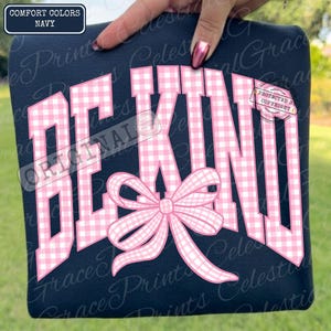 May include: Navy blue sweatshirt with the words "BE KIND" in pink gingham print. A pink bow is centered below the text. The top left corner has a label that says "COMFORT COLORS NAVY".