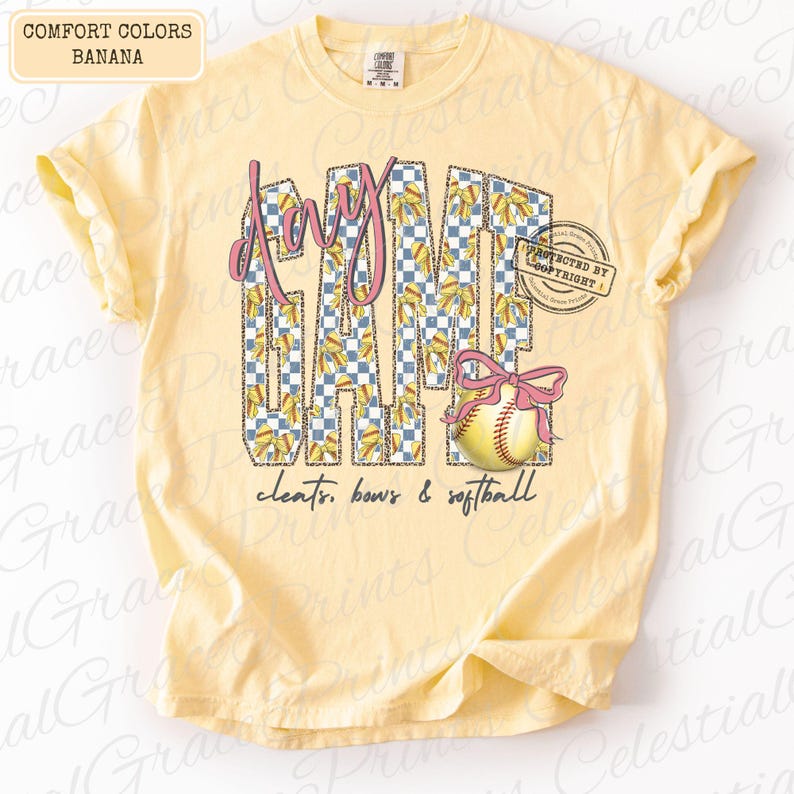 May include: A light yellow t-shirt with the words "Game Day" in a pink and checkered design. A softball with a pink bow is featured below the text, with the words "cleats, bows & softball" below the softball.