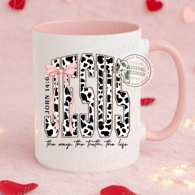 Puede incluir: Taza de cer&aacute;mica blanca con interior y asa rosas. La palabra "JESUS" est&aacute; impresa en la parte delantera con un dise&ntilde;o de estampado de vaca en blanco y negro, con un lazo rosa. Tambi&eacute;n se ve el texto "JOHN 14:6" y "the way, the truth, the life".