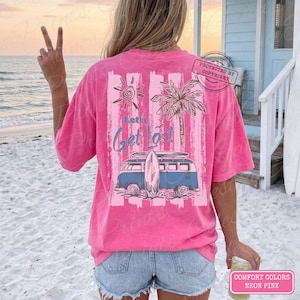May include: Neon pink t-shirt with a beach-themed graphic. The design includes a blue van with a surfboard, a sun, and a palm tree, with the text "Let's Get Lost". The shirt is a Comfort Colors brand.