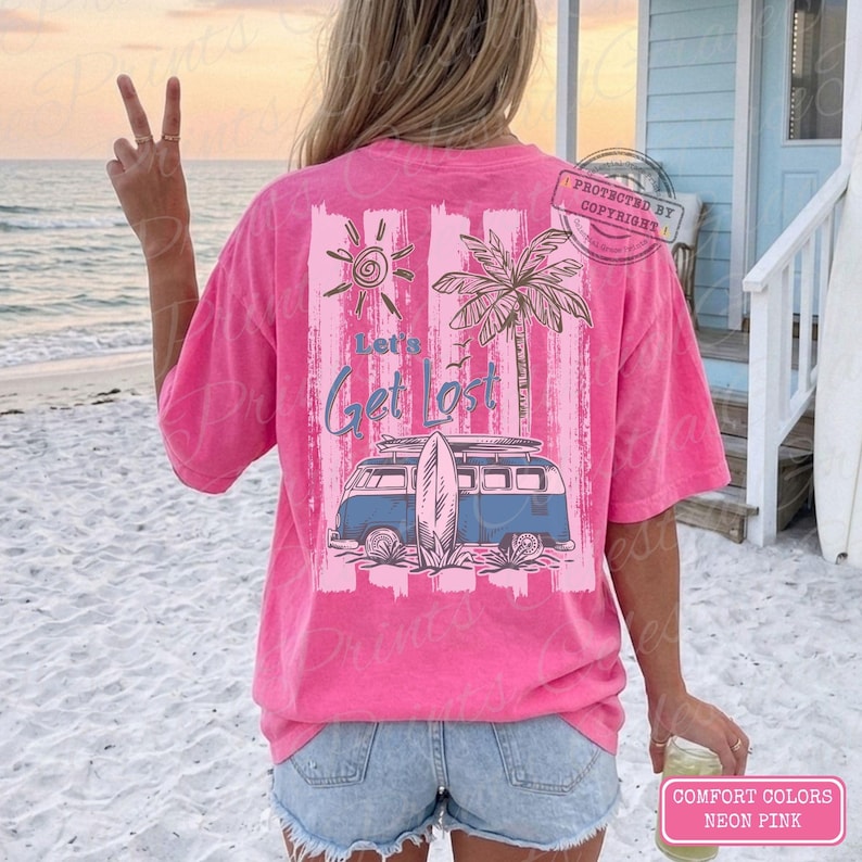 May include: Neon pink t-shirt with a beach-themed graphic. The design includes a blue van with a surfboard, a sun, and a palm tree, with the text "Let's Get Lost". The shirt is a Comfort Colors brand.