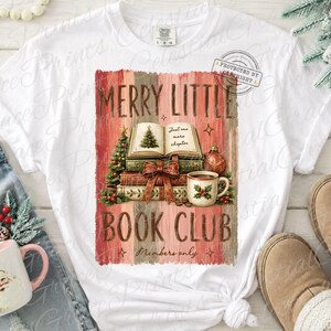 May include: A white t-shirt featuring a graphic of a stack of books, a Christmas tree, and a mug with holly berries. The text reads MERRY LITTLE BOOK CLUB and Members only. The background of the graphic has vertical red and beige stripes.