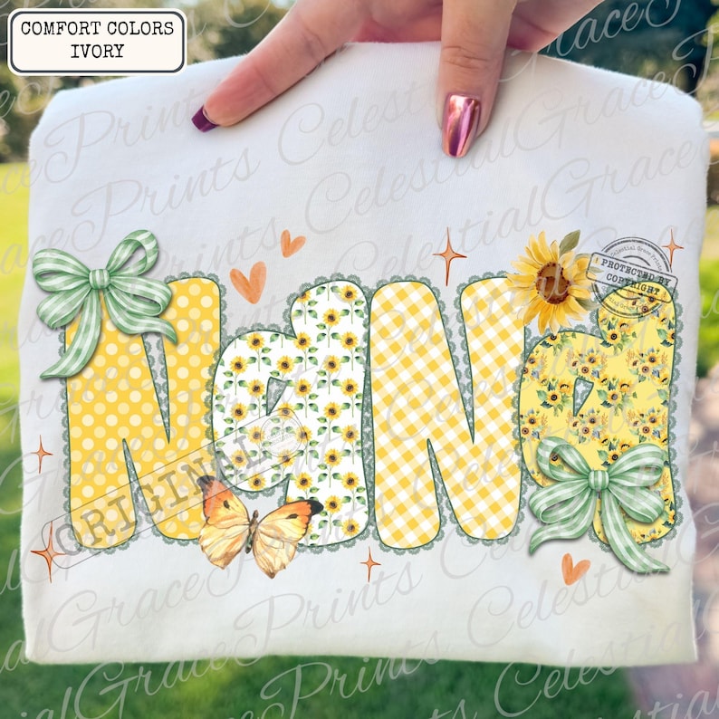 May include: Ivory-colored t-shirt with the word "NANA" in large, decorative letters. The letters feature polka dots, sunflowers, and gingham patterns, with green bows and a butterfly. The shirt has the text "COMFORT COLORS IVORY".