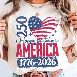 Puede incluir: Camiseta color crema con un dise&ntilde;o patri&oacute;tico. El dise&ntilde;o presenta una bandera estadounidense en forma de coraz&oacute;n, el texto "250 Happy Birthday AMERICA 1776-2026" y el n&uacute;mero "250". El dise&ntilde;o es rojo, blanco y azul.