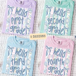 May include: Four pastel-coloured t-shirts with the words "hello first grade", "hello second grade", "hello third grade", and "hello fourth grade" in blue script. Each shirt has a bow, stars, a lightbulb, and a globe graphic.