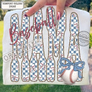 May include: Ivory-colored t-shirt featuring the word "Baseball" in a cursive, red font. The letters are filled with a blue and white checkered pattern and baseball-themed designs. A baseball with a blue bow is also visible.