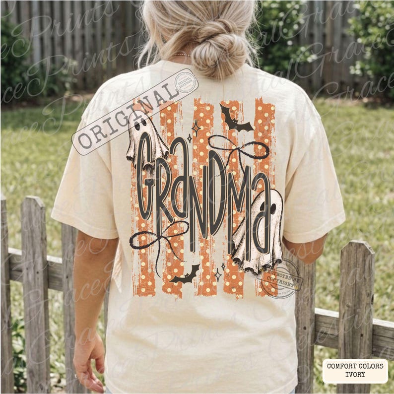 May include: An ivory short-sleeve t-shirt featuring a back graphic with the word GRANDMA in black script. The design includes orange vertical stripes with white polka dots, two white ghost illustrations, black bats, and black bows.