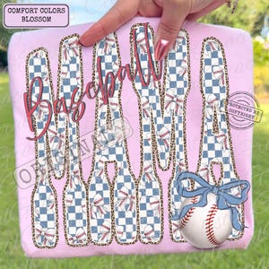 May include: A light pink t-shirt with the word "Baseball" in a cursive font. The word is made up of baseball bats with a blue and white checkered pattern, baseballs, and bows. A baseball with a blue bow is at the bottom.