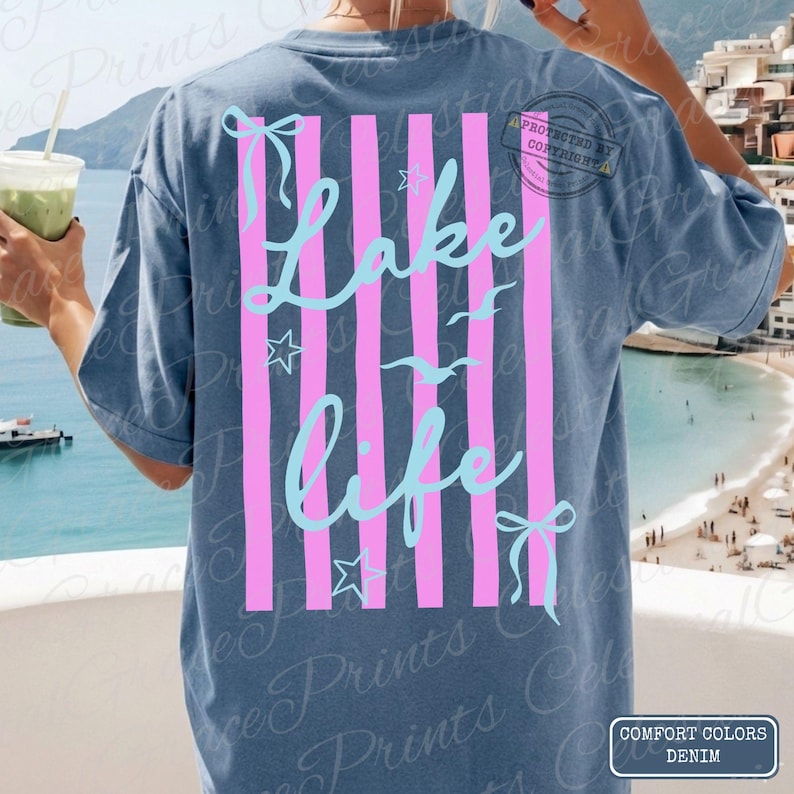 Puede incluir: Camiseta azul denim con un dise&ntilde;o de rayas rosas y blancas. La camiseta presenta las palabras "Lake Life" en una escritura azul claro, junto con estrellas y p&aacute;jaros. La camiseta es de denim Comfort Colors.