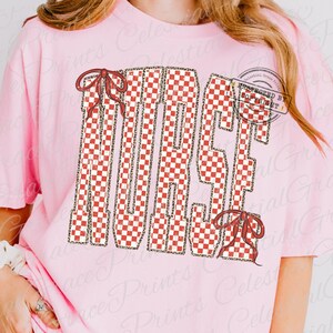 Peut inclure: T-shirt rose clair avec le mot "NICE" en damier rouge et blanc, bord&eacute; d'un imprim&eacute; l&eacute;opard. Le mot est orn&eacute; de deux n&oelig;uds rouges. Le t-shirt est de style d&eacute;contract&eacute;.