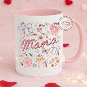 May include: White ceramic mug with a pink interior and handle. The mug features the word "Mama" in pink script, surrounded by floral and bow illustrations, and words like "Wise," "Kind," and "Loved." A circular stamp reads "Original Designer."