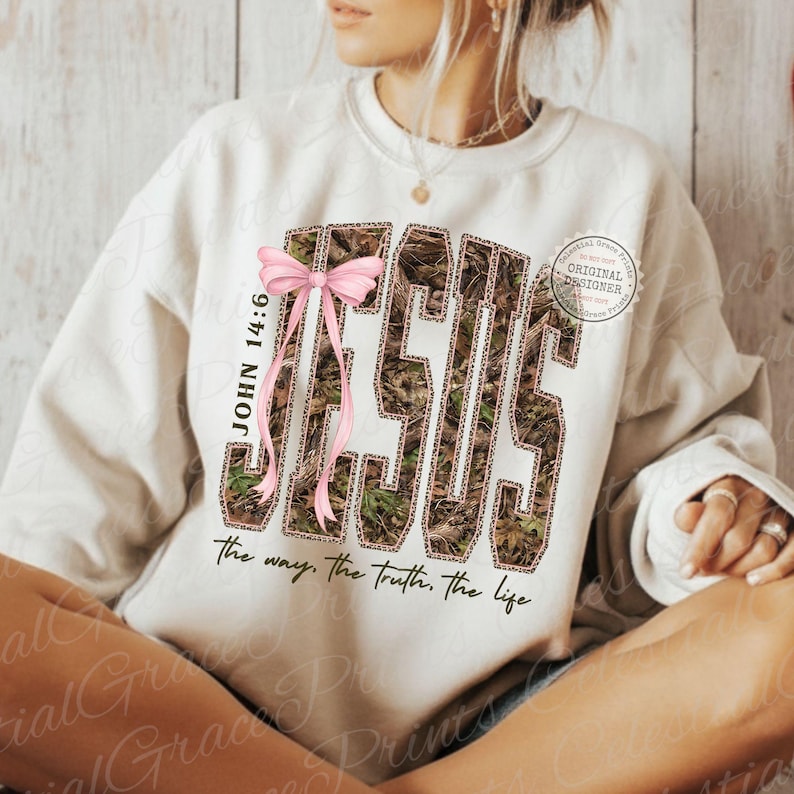 May include: Cream-colored sweatshirt with the word "JESUS" in a camouflage pattern, accented with a pink bow and the text "JOHN 14:6." Below, the sweatshirt reads "the way, the truth, the life."