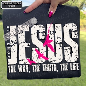May include: Black t-shirt featuring the word "JESUS" in large white distressed letters, with the text "THE WAY, THE TRUTH, THE LIFE." Pink birds are depicted in flight. The shirt also has the text "JOHN 6:9" and "ORIGINAL" on it.
