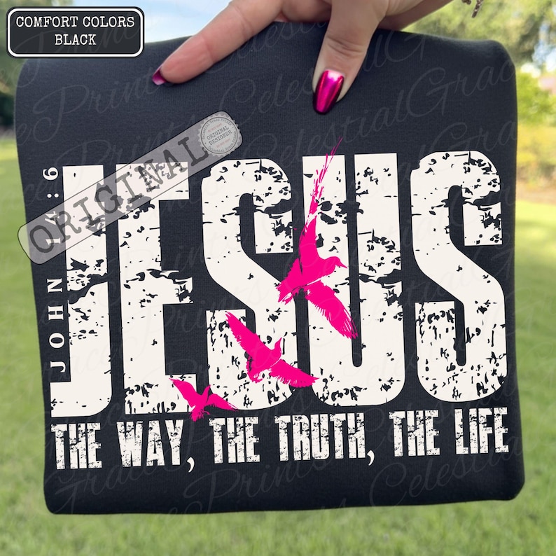 May include: Black t-shirt featuring the word "JESUS" in large white distressed letters, with the text "THE WAY, THE TRUTH, THE LIFE." Pink birds are depicted in flight. The shirt also has the text "JOHN 6:9" and "ORIGINAL" on it.