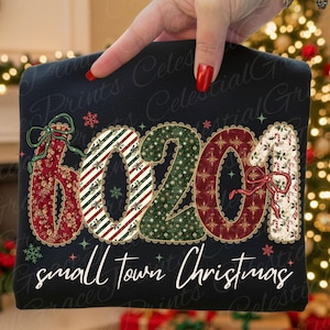Puede incluir: Sudadera negra con el texto "6020" en colores y patrones festivos, incluyendo floral rojo, verde con estrellas doradas y rayas de bastones de caramelo. Las palabras "small town Christmas" están escritas en blanco.