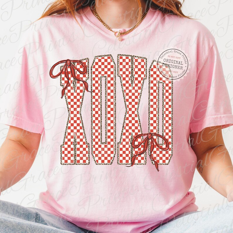 May include: A light pink t-shirt featuring the letters "XXIX" in a red and white checkered pattern with leopard print accents. The letters are adorned with red bows. A circular logo with the text "Celestial Grace Prints" is visible.