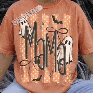 Pu&ograve; includere: Una t-shirt color arancio bruciato con una stampa grafica che riporta la parola MAMA in grandi lettere nere. Il design include due fantasmi bianchi, pipistrelli neri, un fiocco nero e strisce verticali con pois bianchi su sfondo arancione chiaro.