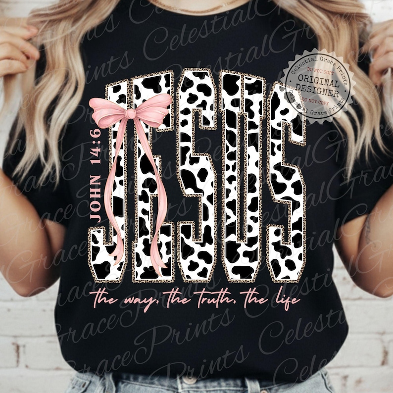 Puede incluir: Camiseta negra con la palabra "JESUS" en un dise&ntilde;o de estampado de vaca, acentuada con un lazo rosa. El texto "JOHN 14:6" est&aacute; a la izquierda, y "the way, the truth, the life" est&aacute; en la parte inferior.