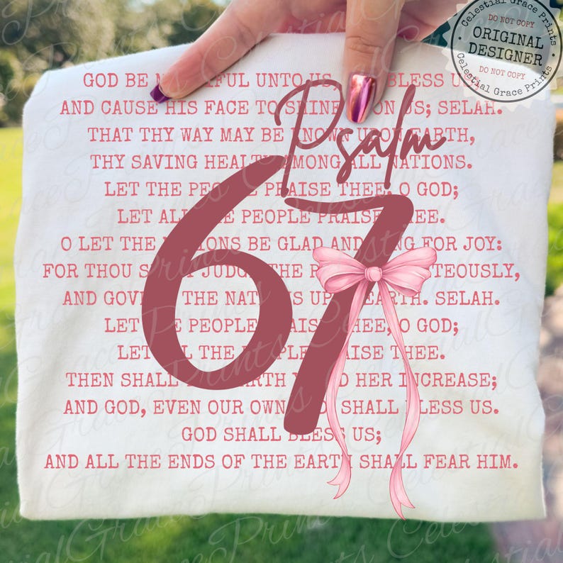 May include: A white t-shirt with the text of Psalm 67 in a burgundy color. A pink bow is attached to the right side of the number 67. The words "Celestial Grace Prints" are printed on the top right corner.
