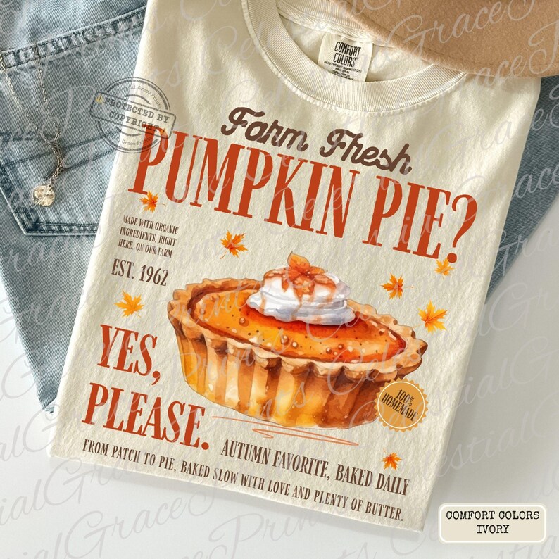 May include: An ivory t-shirt featuring a graphic of a pumpkin pie with whipped cream, surrounded by orange maple leaves. Text reads: Farm Fresh PUMPKIN PIE? EST. 1962 YES, PLEASE. MADE WITH ORGANIC INGREDIENTS, RIGHT HERE, ON OUR FARM. AUTUMN FAVORITE, BAKED DAILY.