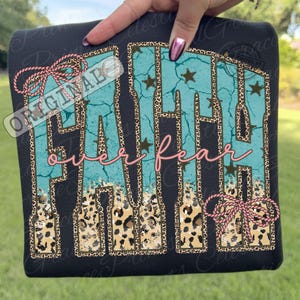 May include: Black sweatshirt with the words "FAITH over fear" in turquoise, leopard print, and pink script. The word "FAITH" has a turquoise background with brown stars. The sweatshirt has a pink bow on the top left and bottom right.