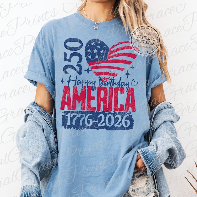 Puede incluir: Camiseta azul claro con el texto "250 Happy Birthday AMERICA 1776-2026". El dise&ntilde;o incluye una bandera americana en forma de coraz&oacute;n. La camiseta tiene mangas enrolladas y se usa con una chaqueta vaquera.