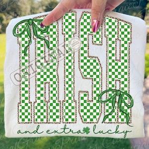 May include: White t-shirt with the words "IRISH" in large green and white checkered letters, outlined with a brown leopard print. Green bows and a shamrock accent the design. The text "and extra lucky" is written in green.