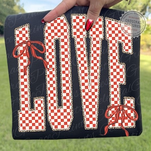 May include: Black sweatshirt with the word "LOVE" in large, bold letters. The letters have a red and white checkered pattern with a leopard print border. Red bows are on the top and bottom of the word.