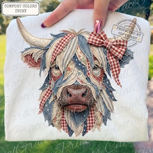 May include: Ivory-colored t-shirt featuring a detailed appliqué of a Highland cow. The cow's face is crafted from fabric scraps in red, blue, and cream patterns, including stars and gingham. A red gingham bow adorns the cow's head. The text "COMFORT COLORS IVORY" is in the upper left corner.