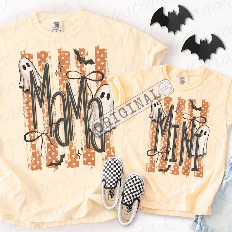 May include: Two pale yellow t-shirts featuring a graphic print with orange polka-dot stripes, black bats, and white ghosts. The larger shirt displays the text MAMA in black, while the smaller shirt displays the text MINI in black. Both shirts include black bow accents.