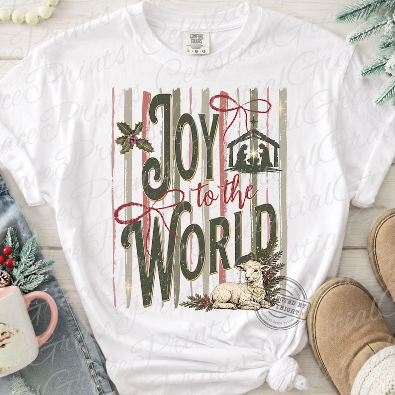 Puede incluir: Una camiseta blanca de manga corta con un estampado gr&aacute;fico que incluye el texto Joy to the World en verde oscuro y rojo. El dise&ntilde;o presenta una silueta de bel&eacute;n, un peque&ntilde;o cordero, hojas de acebo y rayas verticales en tonos apagados.