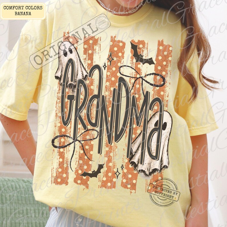 May include: A pale yellow short-sleeve t-shirt featuring a graphic print with the word GRANDMA in large black script. The design includes two white ghosts, black bats, and a background of vertical orange stripes with white polka dots.