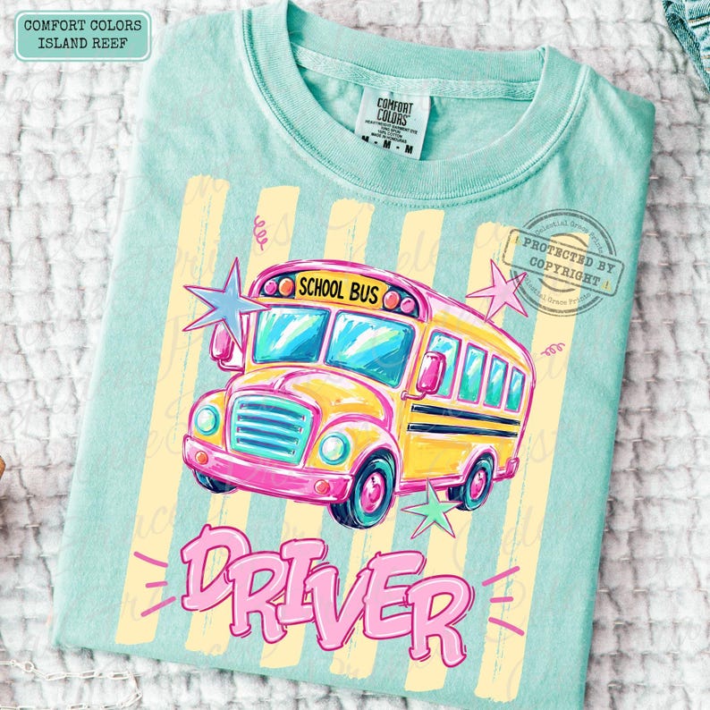 May include: A light teal t-shirt featuring a yellow school bus graphic with the text "SCHOOL BUS" above the windshield and "DRIVER" in large pink letters below. The design includes light yellow vertical stripes and pink and blue star accents.
