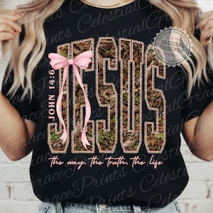 May include: Black t-shirt with the word "JESUS" in a camouflage and leopard print design. A pink bow and the text "JOHN 14:6" are on the left side. The phrase "the way, the truth, the life" is at the bottom.