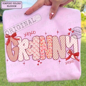 May include: A light pink sweatshirt with the word "GRANNY" in a decorative font. The letters are filled with heart patterns and trimmed with a scalloped edge. Red bows and the text "xoxo" are also featured.