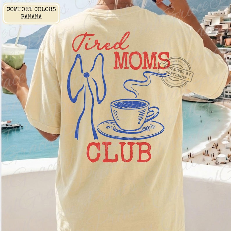 May include: Banana-colored t-shirt with a graphic design on the back. The design features the words "Tired Moms Club" in red, a blue bow, and a blue and white coffee cup. The shirt also has the words "Comfort Colors" and "Banana" in the upper left corner.