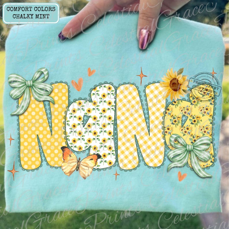 May include: A light blue t-shirt with the word "NANA" in large, decorative letters. The letters feature yellow polka dots, sunflower patterns, and gingham. A butterfly and bows add to the design. The shirt is labeled "Comfort Colors Chalky Mint."