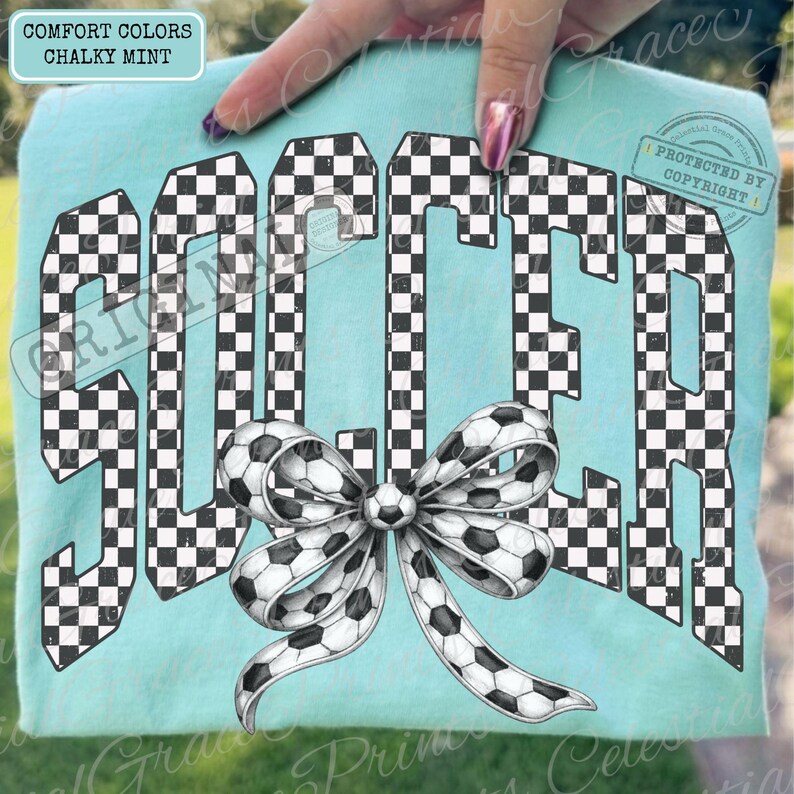 May include: A light blue t-shirt with the word "SOCCER" in a black and white checkered pattern. A soccer ball bow is centered below the word. The shirt has the words "COMFORT COLORS" and "CHALKY MINT" in the upper left corner.