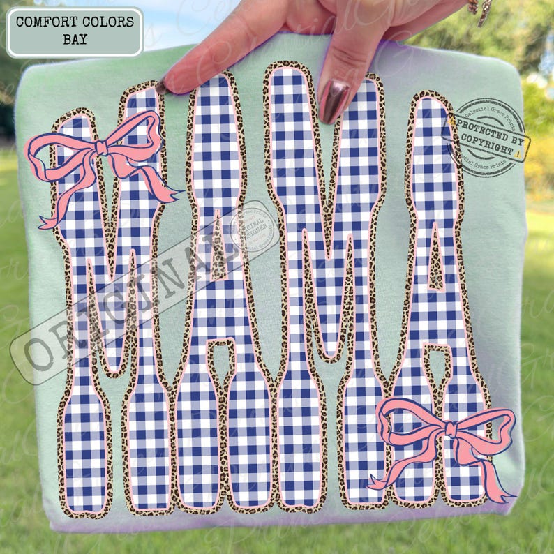 May include: A light green Comfort Colors sweatshirt featuring the word "MAMA" in a navy and white gingham pattern, outlined with leopard print. Pink bows are included in the design.
