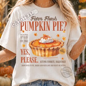 May include: An off-white t-shirt featuring a graphic of a pumpkin pie with whipped cream, surrounded by orange maple leaves. Text reads: Farm Fresh PUMPKIN PIE? EST. 1962 YES, PLEASE. AUTUMN FAVORITE, BAKED DAILY. FROM PATCH TO PIE, BAKED SLOW WITH LOVE.