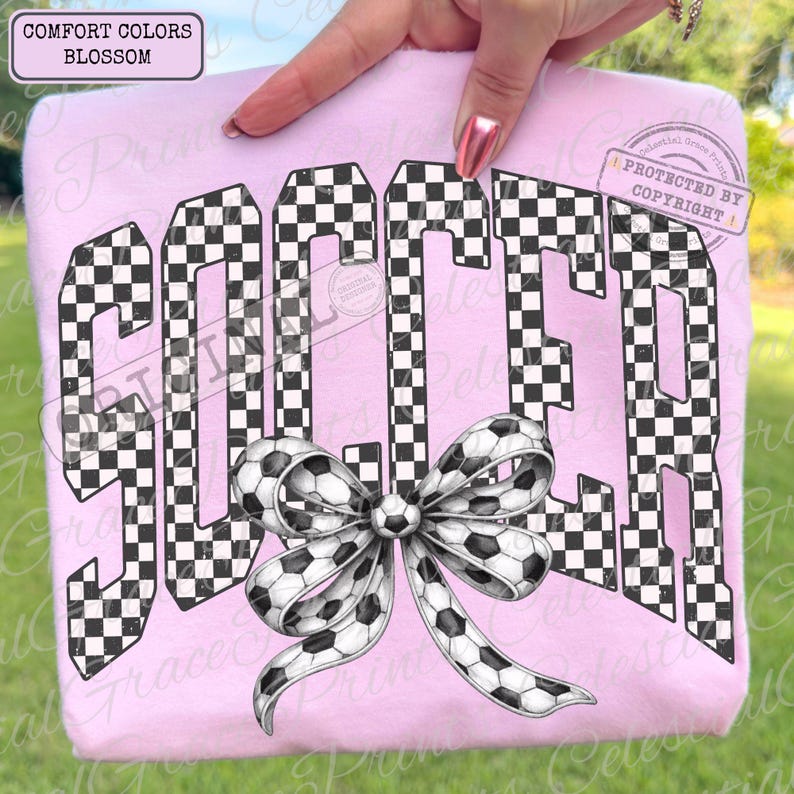 May include: A light pink sweatshirt with the word "SOCCER" in large, checkered letters. A bow made of soccer ball print ribbon is at the bottom of the word. The top left corner has the words "COMFORT COLORS BLOSSOM".