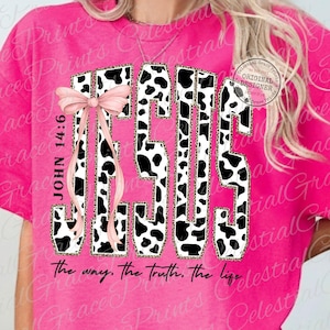 Puede incluir: Camiseta rosa intenso con la palabra "JESUS" en un dise&ntilde;o de letras en bloque audaz. Las letras presentan un patr&oacute;n de vaca con un borde de estampado de leopardo. Un lazo rosa y el texto "JOHN 14:6" est&aacute;n en el lado izquierdo. La frase "the way, the truth, the life" est&aacute; en la parte inferior.